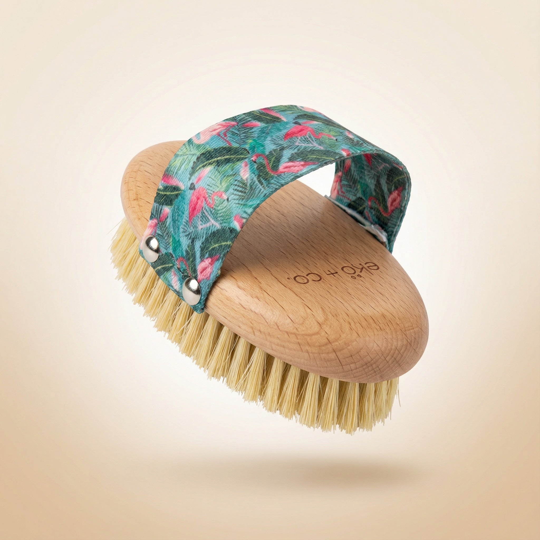 dry body brush shown at angle displaying natural sisal bristles and beechwood handle with flamingo strap arched over top