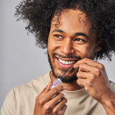 huppy dental floss in use - smiling man with curly hair demonstrating proper flossing technique with the glass container, showing daily oral care routine