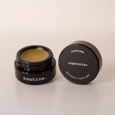 routine Superstar botanic perfume balm - open black glass jar showing golden-yellow solid perfume with black lid displaying product name