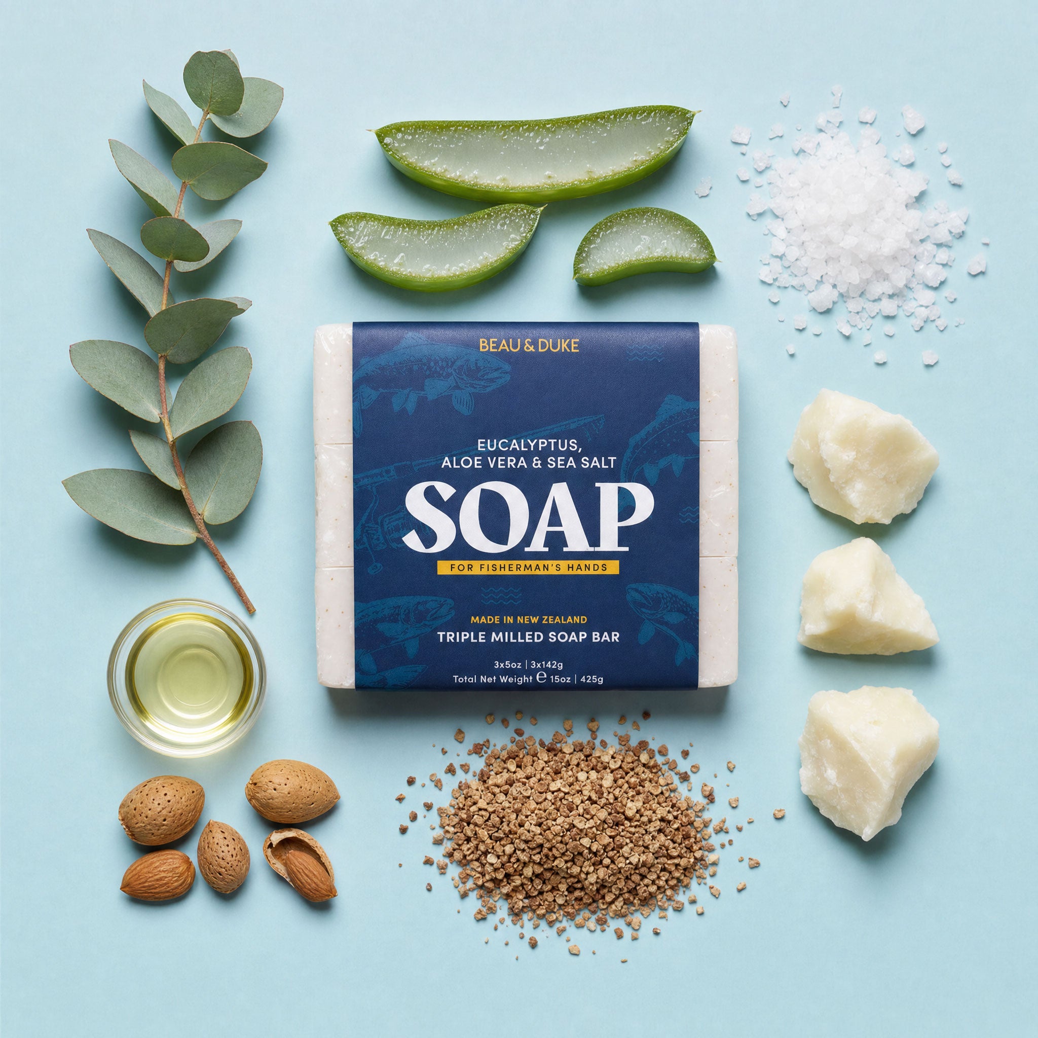 Flat lay of Beau & Duke soap bar surrounded by key ingredients including fresh eucalyptus branch, sliced aloe vera, sea salt crystals, sweet almond oil, raw almonds, ground walnut shell exfoliant, and shea butter chunks on a light blue background