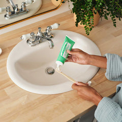 Hands applying Dr. Bronner's Spearmint organic toothpaste to bamboo toothbrush over bathroom sink demonstrating daily natural oral care routineRetry