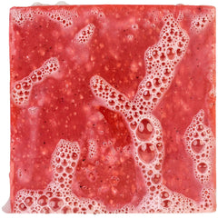 Wet crimson Ruthless Rinse bar soap covered in foamy lather showing dark black-sand exfoliant speckles throughout