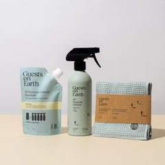 Three eco-friendly cleaning products from 'Guests on Earth' on a beige surface with a light gray background.