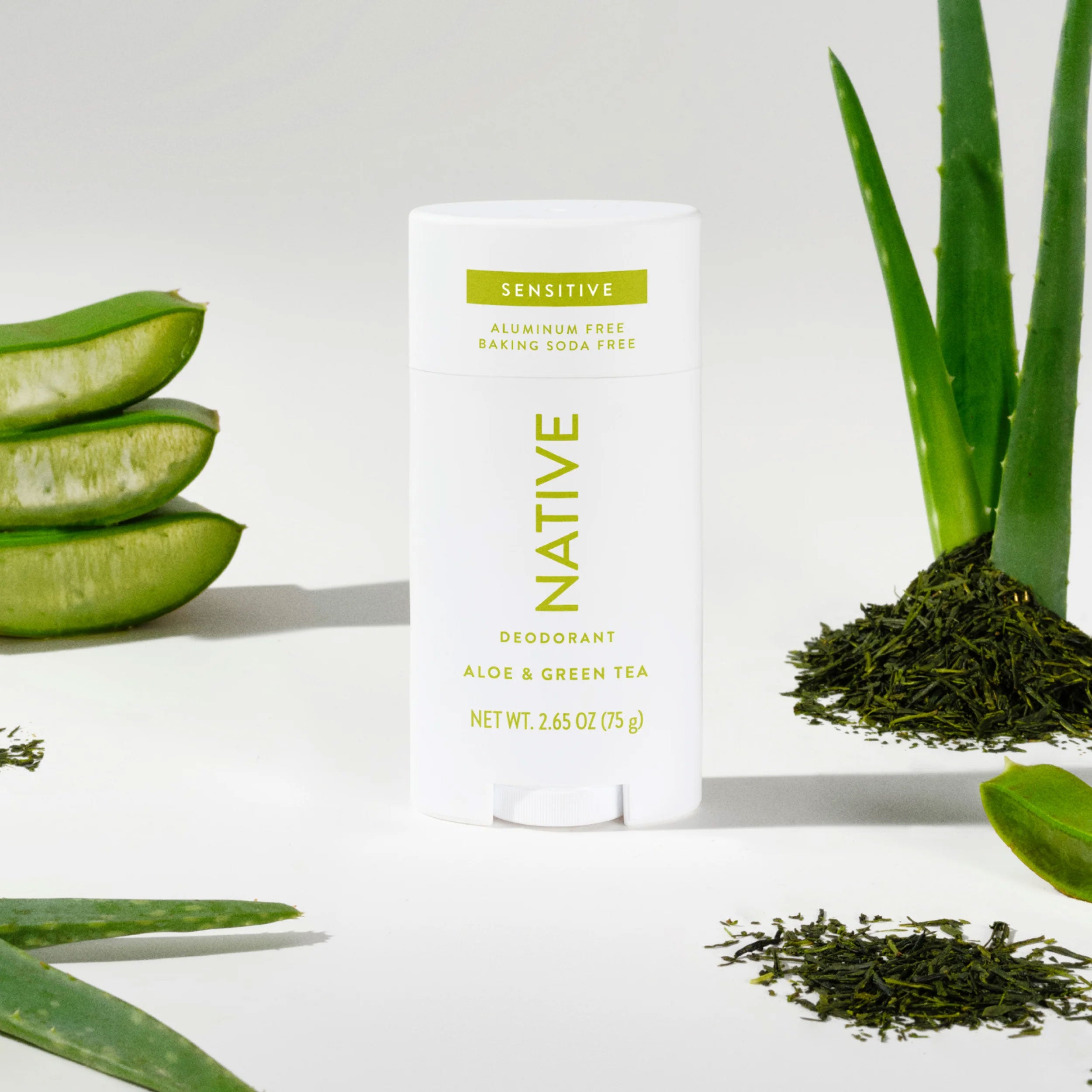 Native Aloe & Green Tea deodorant stick styled with fresh sliced aloe vera leaves and loose green tea leaves on white background