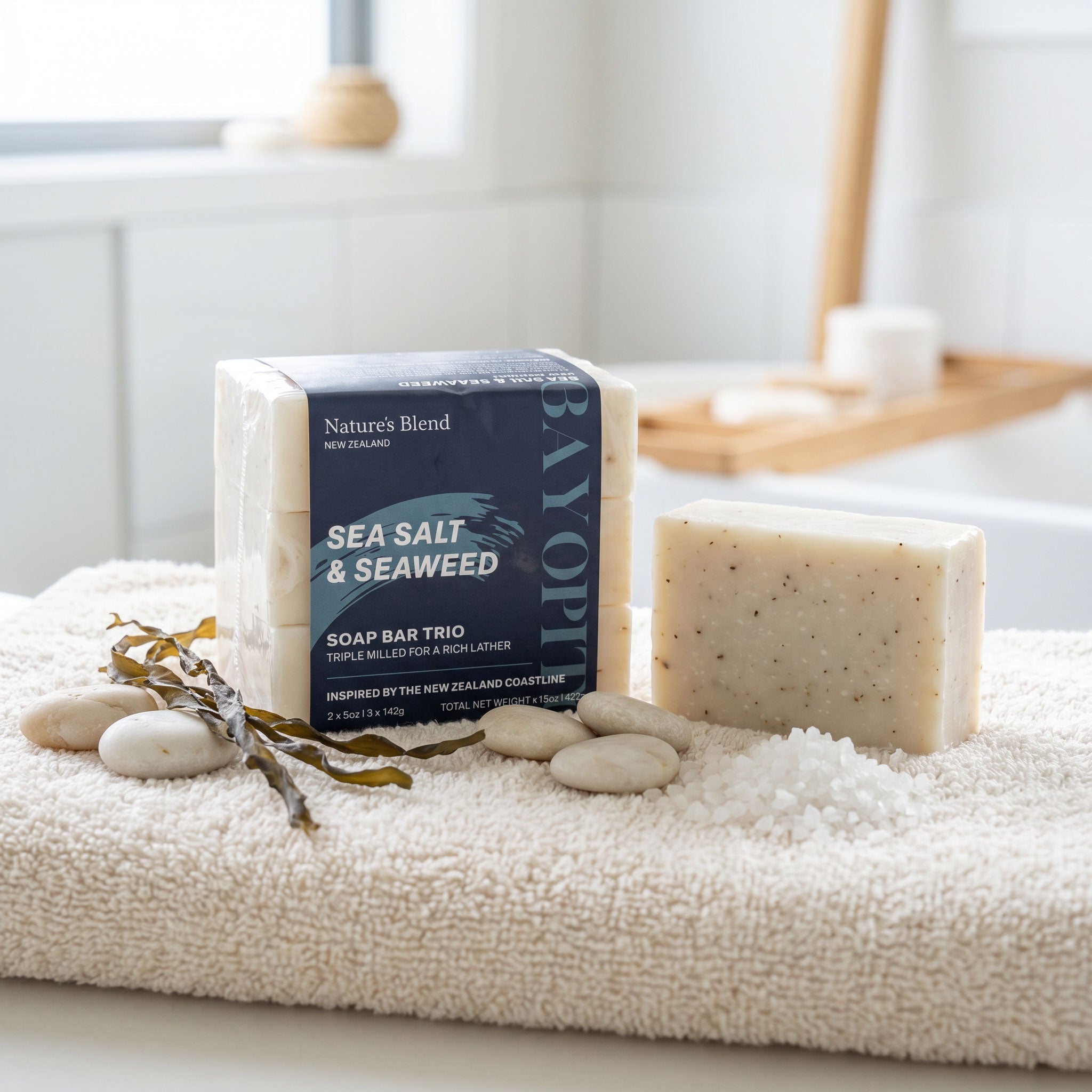 Nature's Blend Sea Salt and Seaweed soap trio displayed on a white bath towel with sea salt, river stones, and dried seaweed alongside a single unwrapped bar