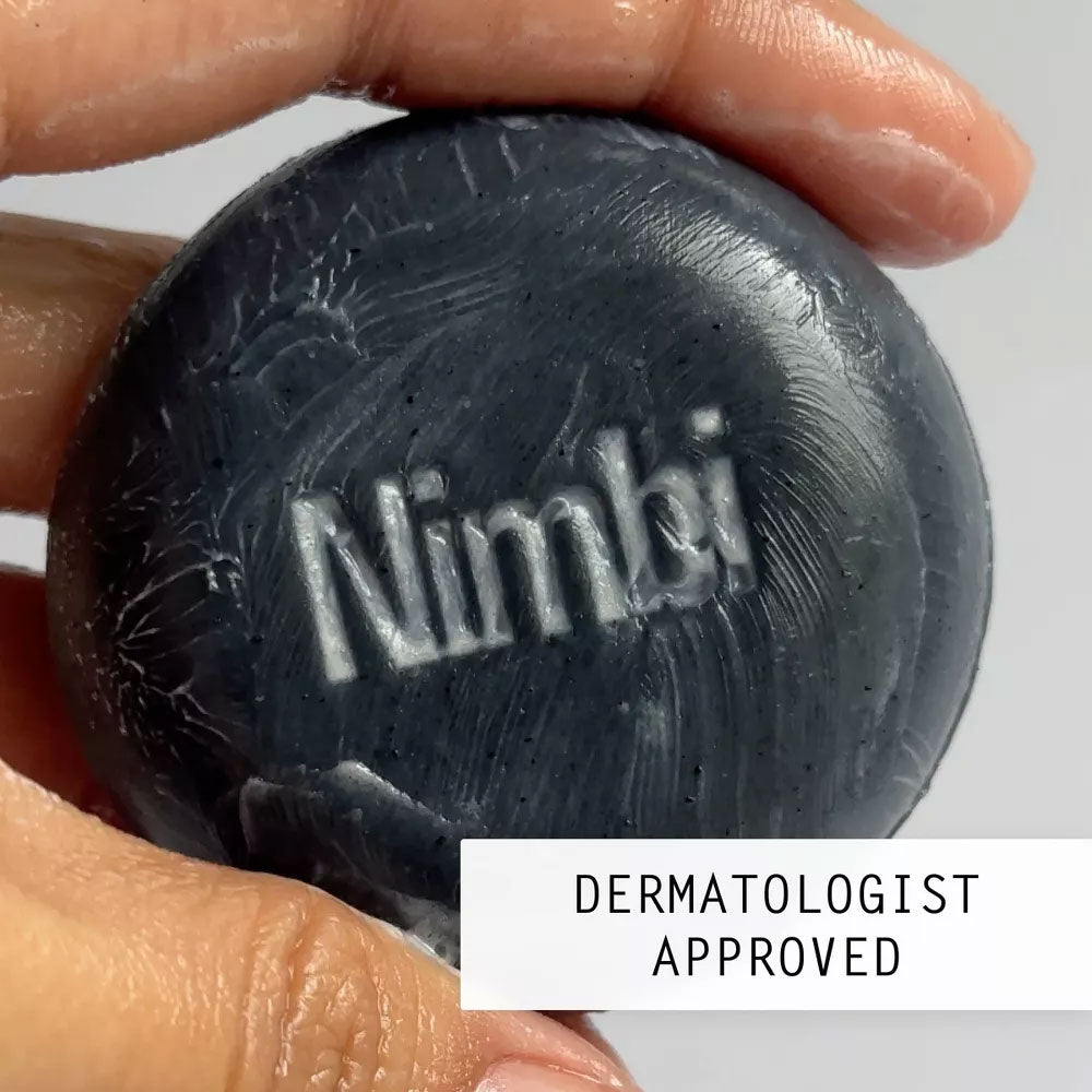 Hand holding wet Nimbi charcoal shave puck with embossed logo, marked Dermatologist Approved