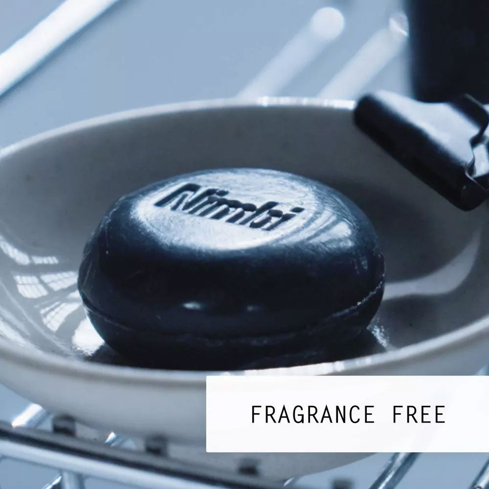 Nimbi charcoal shave puck resting on a wire-rimmed soap dish next to a black safety razor, labelled Fragrance Free