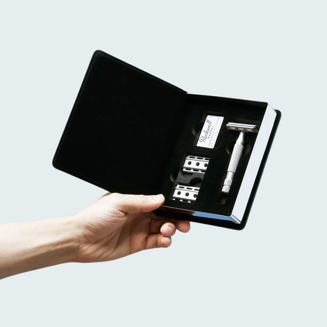 Hand holding the premium black velvet-lined gift box displaying the razor and base plates in protective foam insert