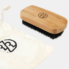 Rockwell beard brush bamboo handle with engraved logo lying on white cotton towel demonstrating sustainable natural wood construction.