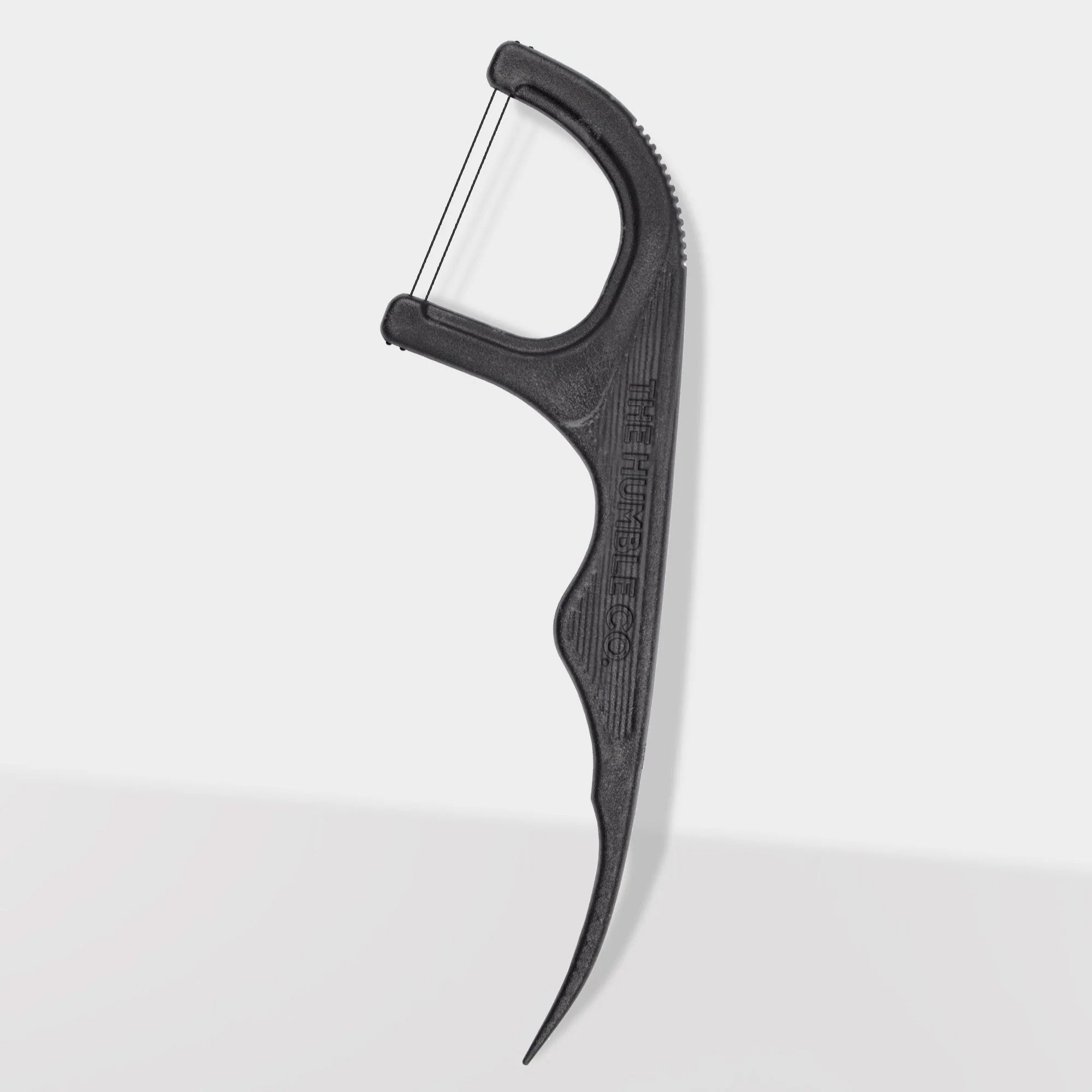 Close-up of The Humble Co. black dental floss pick displaying ergonomic curved handle with textured grip pattern and brand name embossed on side for secure handling