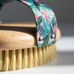 Close-up detail of ekö + co. dry brush flamingo strap attachment showing metal snaps and natural bristle texture with beechwood grain visible