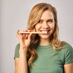Smiling woman in green shirt holding huppy bamboo toothbrush horizontally near her mouth, demonstrating comfortable grip and natural feel