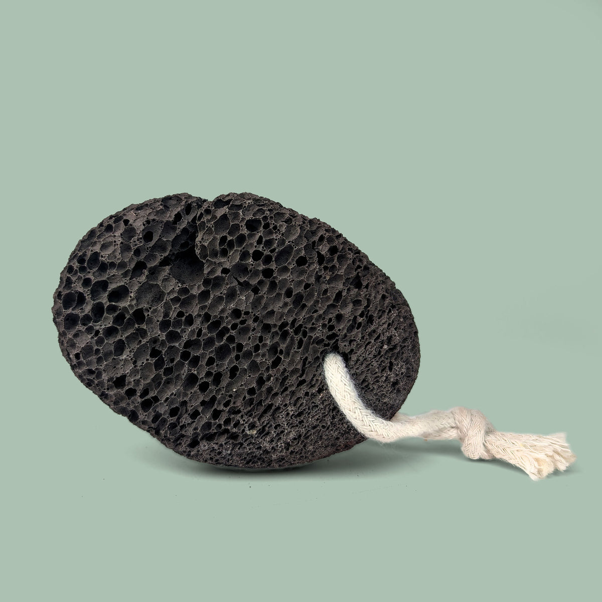 Black natural pumice stone with a rope on a light green background