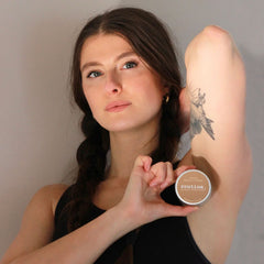 Young woman with tattoo holding Routine Bonnie N' Clyde deodorant jar demonstrating product size and natural skincare application for underarm use