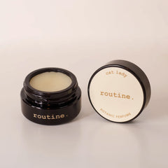 Routine Cat Lady botanic perfume balm - open black glass jar showing cream-coloured solid perfume with detached lid displaying product name - natural moisturizing fragrance balm