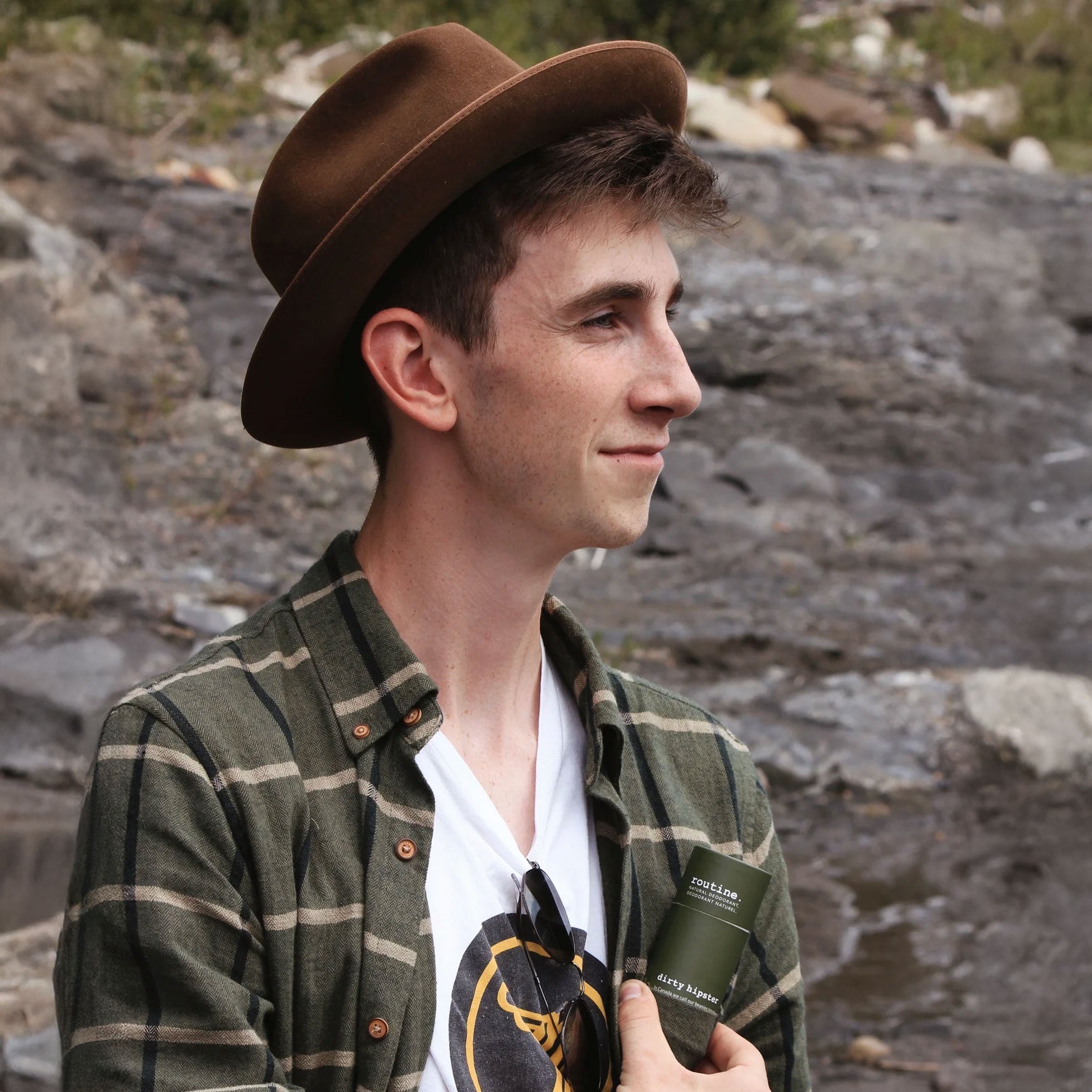 Outdoor lifestyle shot of man wearing flannel holding Routine deodorant stick in natural wilderness setting