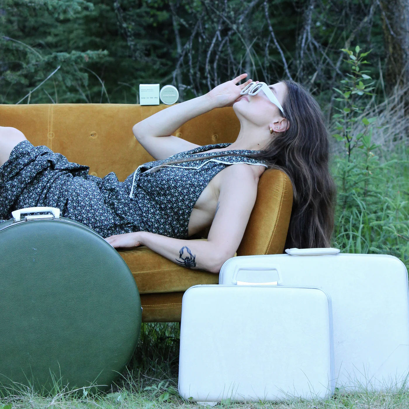 Woman relaxing outdoors with Routine Lucy in the Sky deodorant jar on vintage suitcase showing lifestyle use of natural deodorant in travel setting