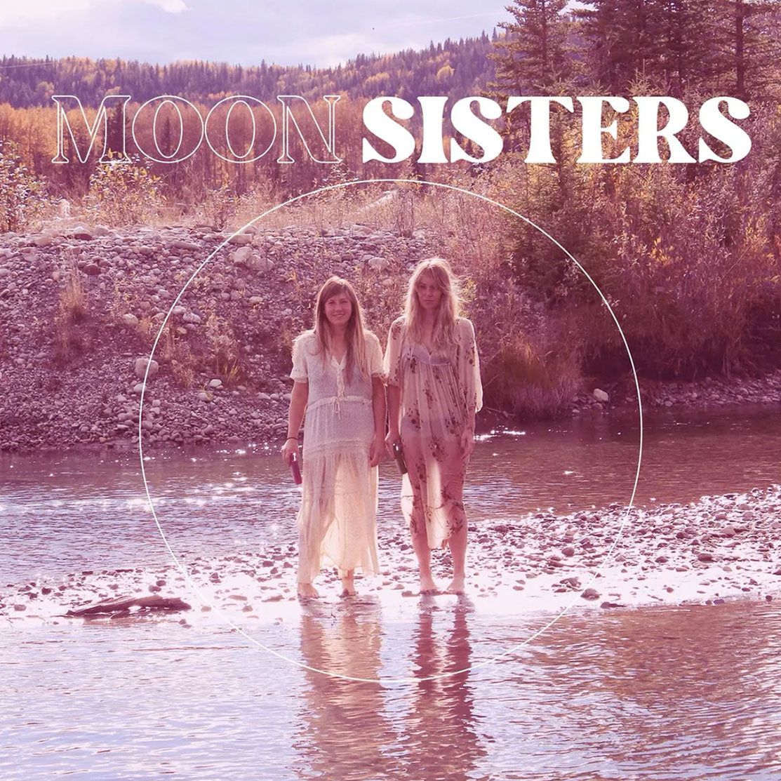 Moon Sisters brand imagery - two women in bohemian dresses standing by water with mountain landscape - representing natural, feminine lifestyle and floral deodorant inspiration