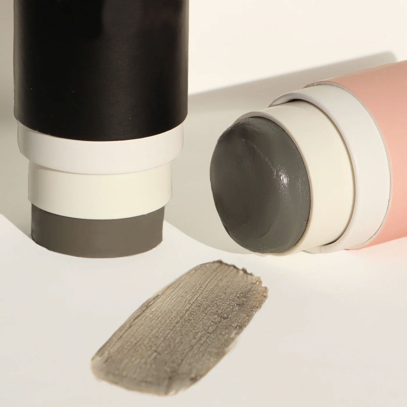 Routine Superstar deodorant with its cap removed, revealing the dark-grey charcoal stick beside a swatch of its creamy texture on a beige-toned surface.