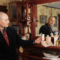 A man holding The Curator deodorant stick in a vintage bedroom setting showing sustainable paper packaging.