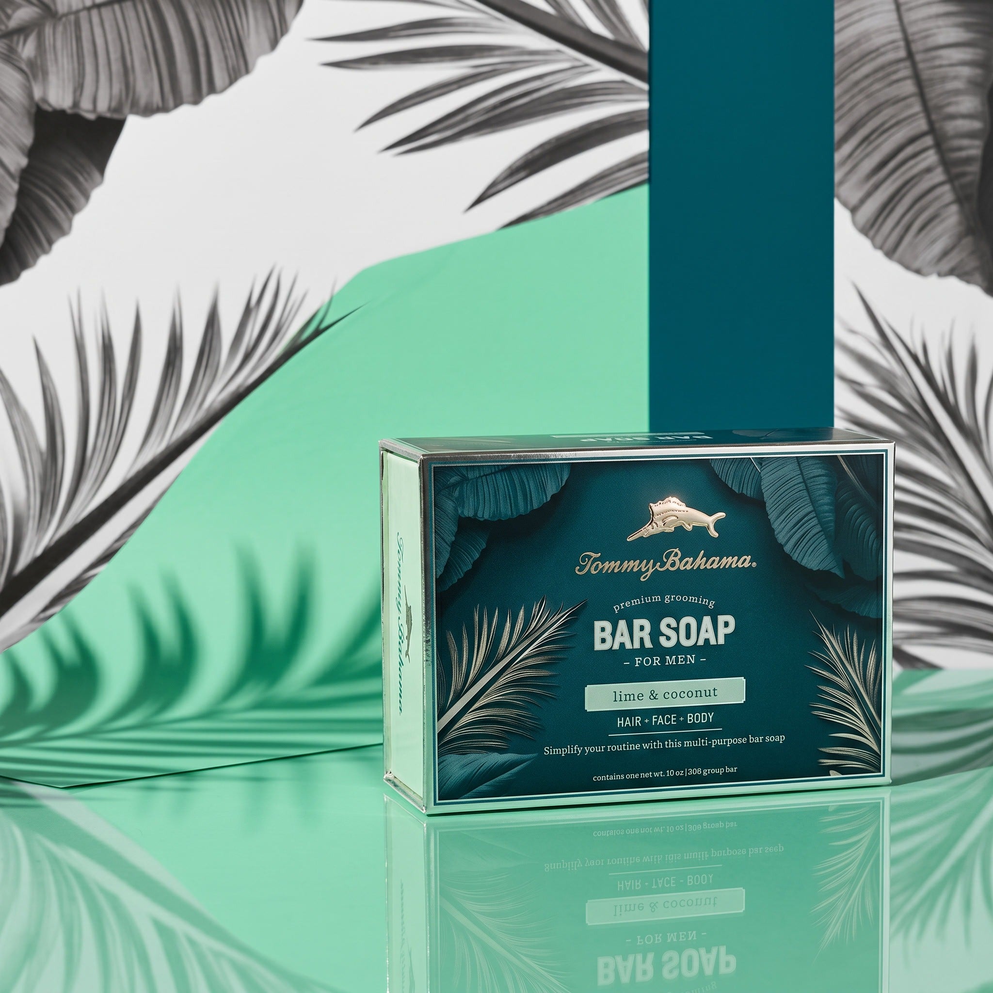 Tommy Bahama Lime & Coconut Bar Soap gift box displayed on a reflective teal surface with palm leaf shadows and tropical green backdrop